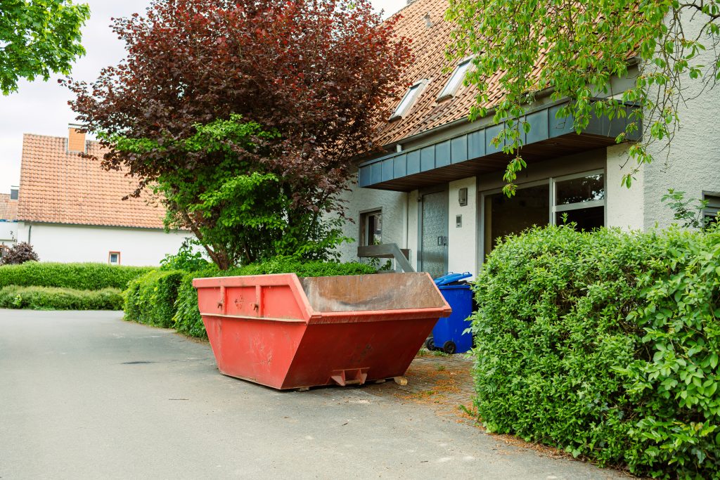 large street garbage container. metal red container for construction waste. garbage container standing near the house during renovation.